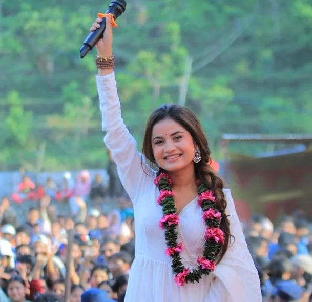 Nepali singer Eleena Chauhan performing on stage with a garland and microphone raised in front of a cheering crowd
